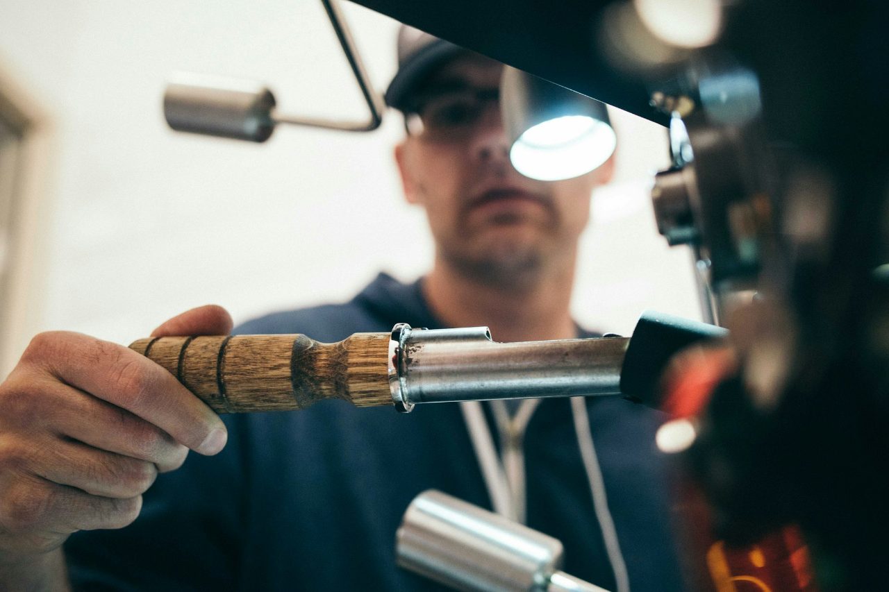 A machinist guiding a wooden-handled lathe tool past a machine in a workshop